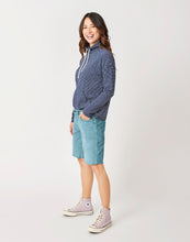 Side view of Woman wearing light blue jean shorts and the navy blue stripe Bodie funnel Neck, Carve Designs
